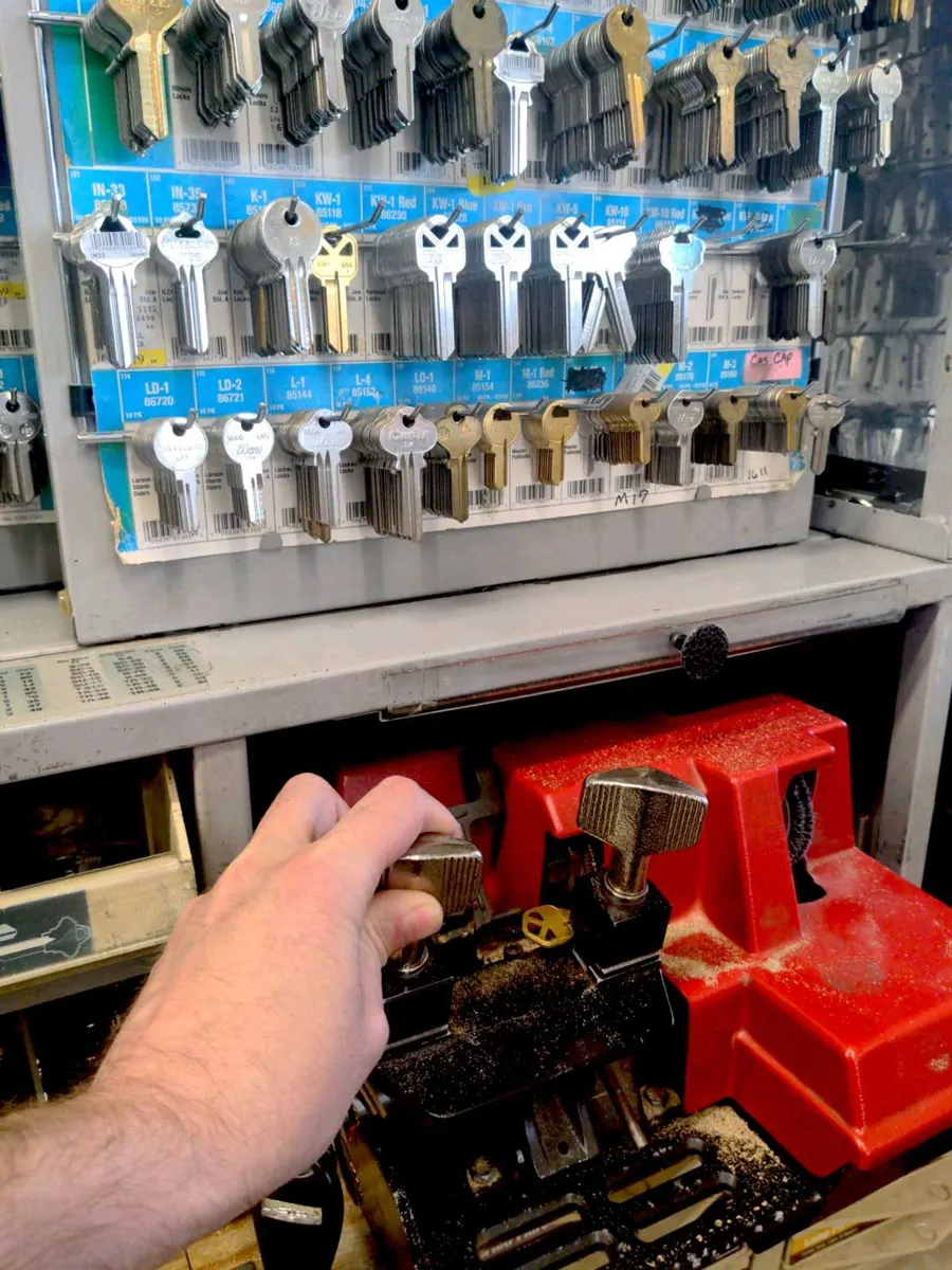 A key being cut on the machine, with the wall of key blanks behind